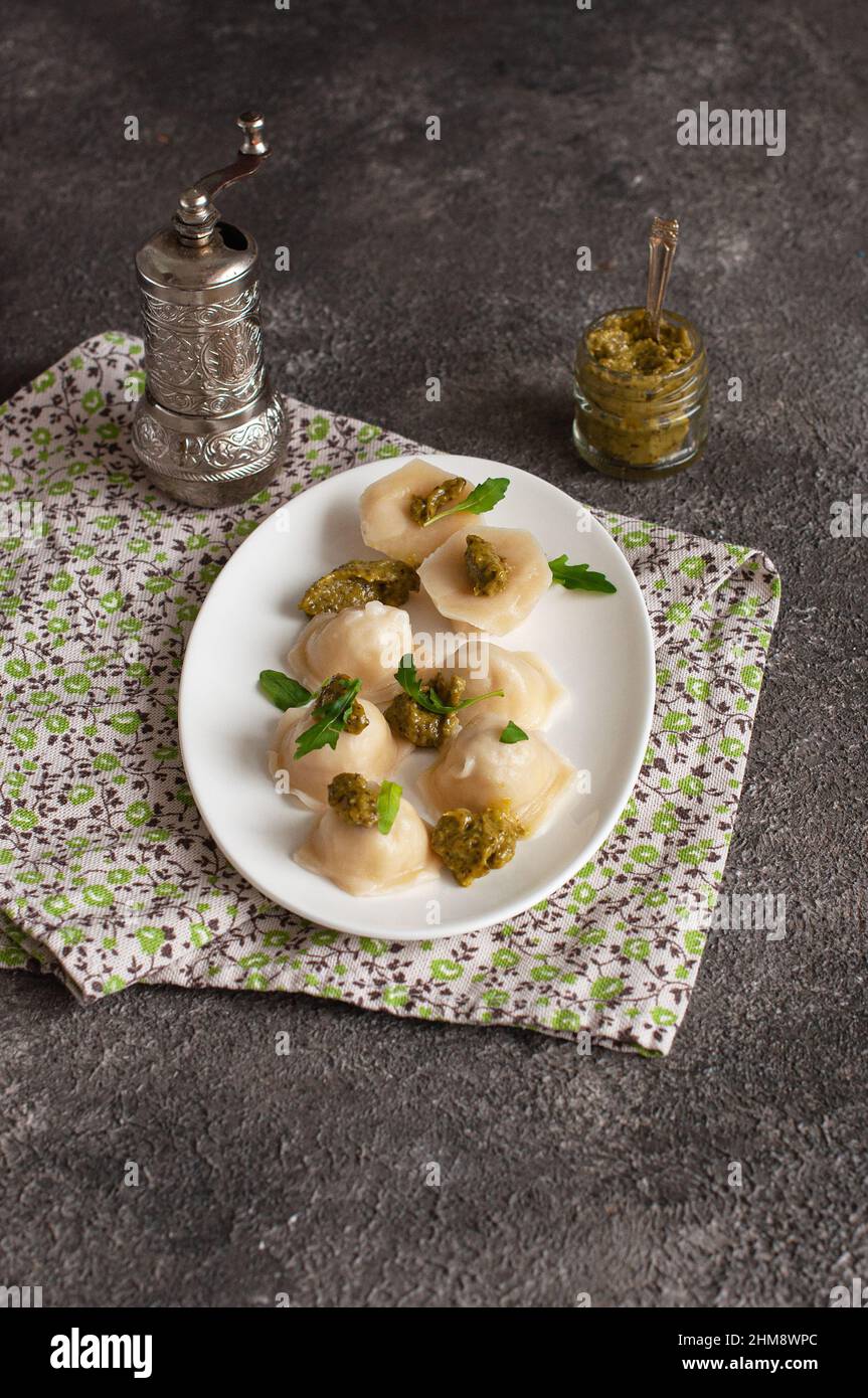 Homemade ravioli stuffed with chicken meat  and pesto sauce in a white plate on a grey background. Stock Photo