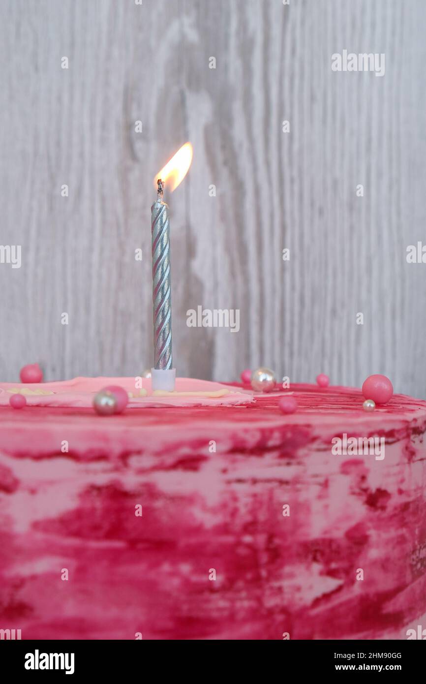 Side view of colorful pink birthday cake with one burning candle. Party