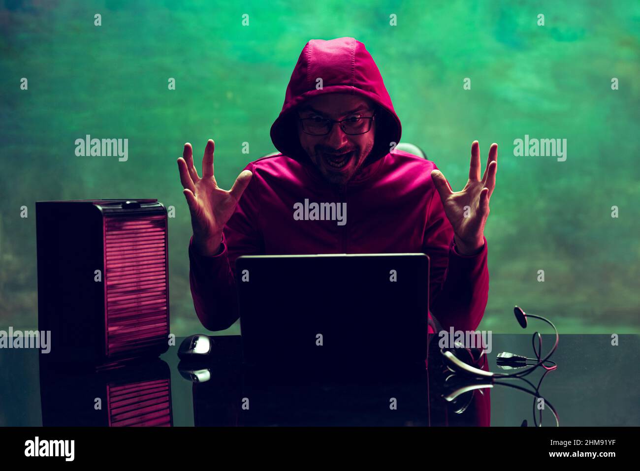 Portrait of man, computer geek, hacker working with laptop, breaking security system isolated over dark green background in neon Stock Photo