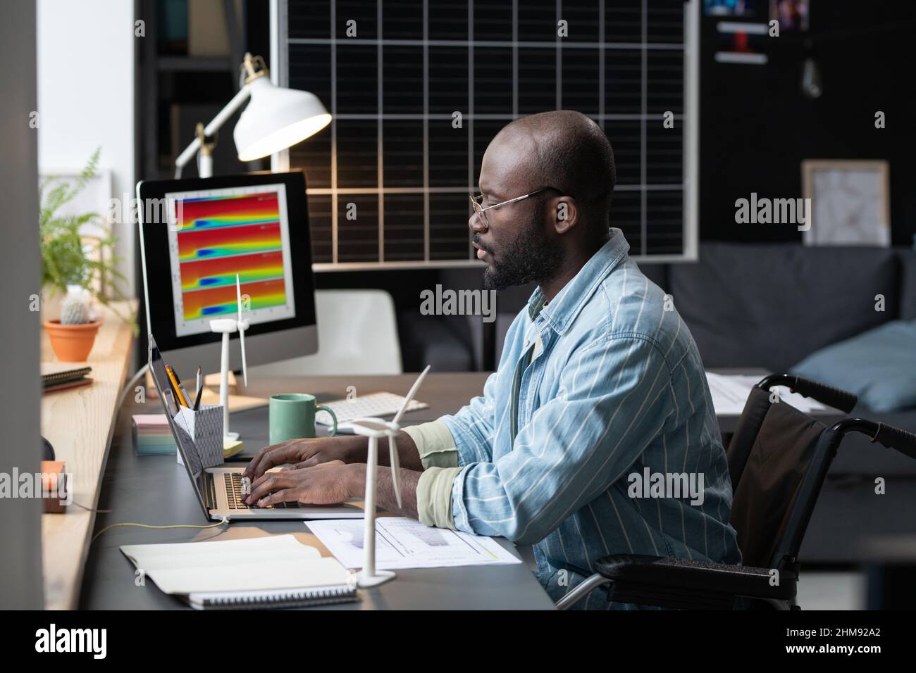 African architect with disability sitting at his workplace and typing ...