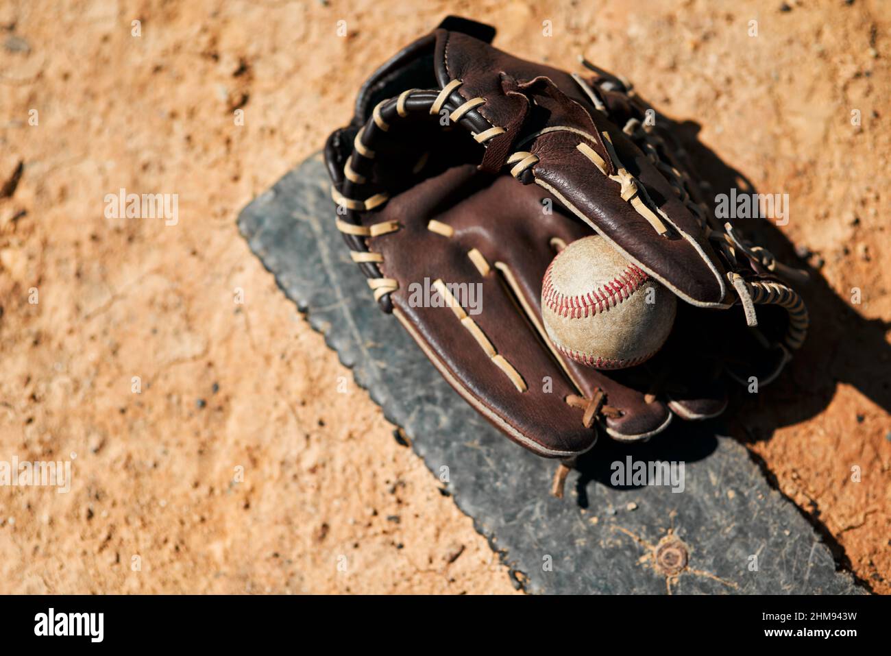 Its baseball season. Shot of a baseball mitt and ball lying on the pitch during the day. Stock Photo