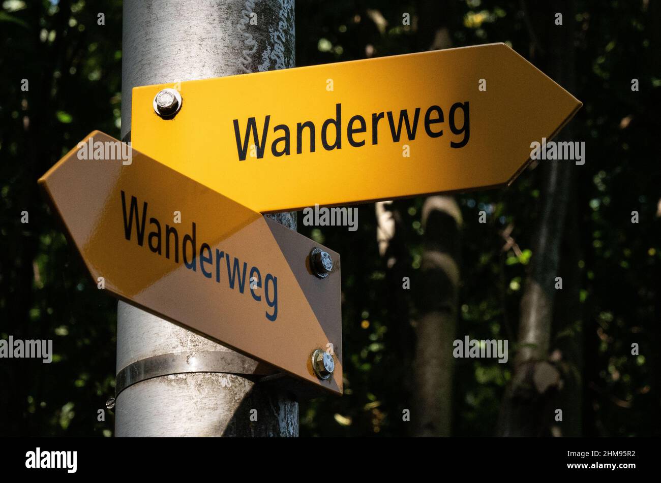 Swiss yellow hiking trail signs with black text, in german 'Wanderweg', lit partially by sunlight and partially covered in shadow. Stock Photo