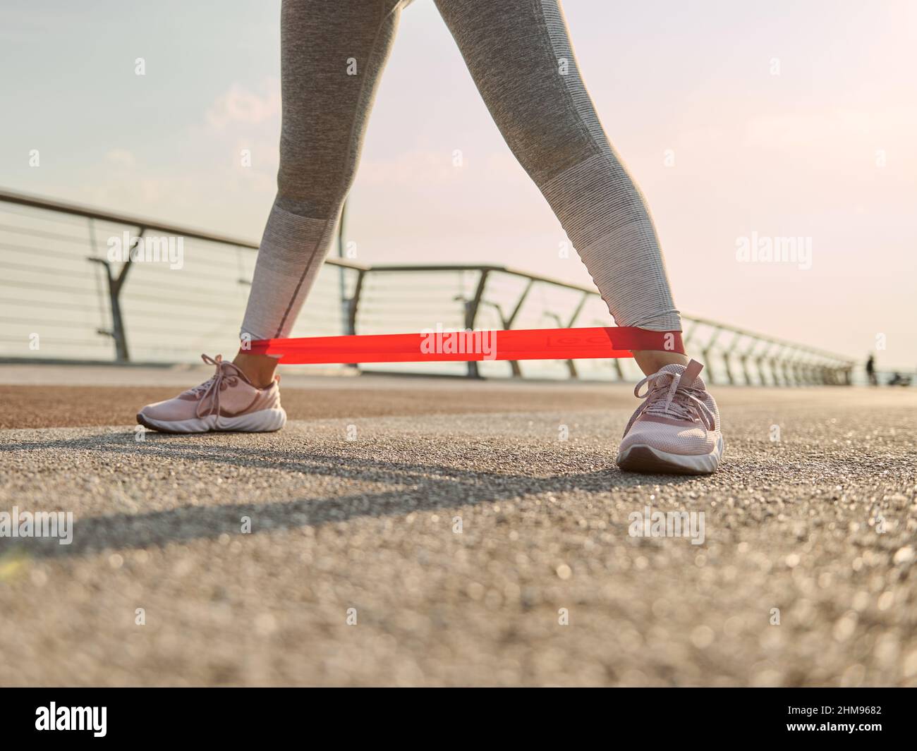 Close-up. Croped image of the legs of an athlete woman, sportswoman in gray leggins doing body weight training, exercising with a resistance fitness e Stock Photo