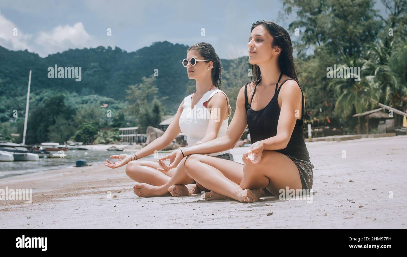 Young woman doing yoga pose on beach in summertime in lotus position ...