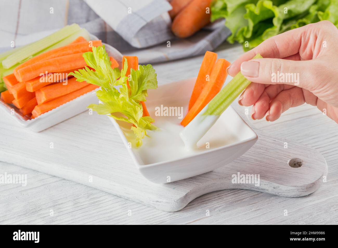 Vegetable sticks. Fresh celery and carrot with yogurt sauce. Woman's Hand holding celery stick. Healthy and diet food concept. Stock Photo