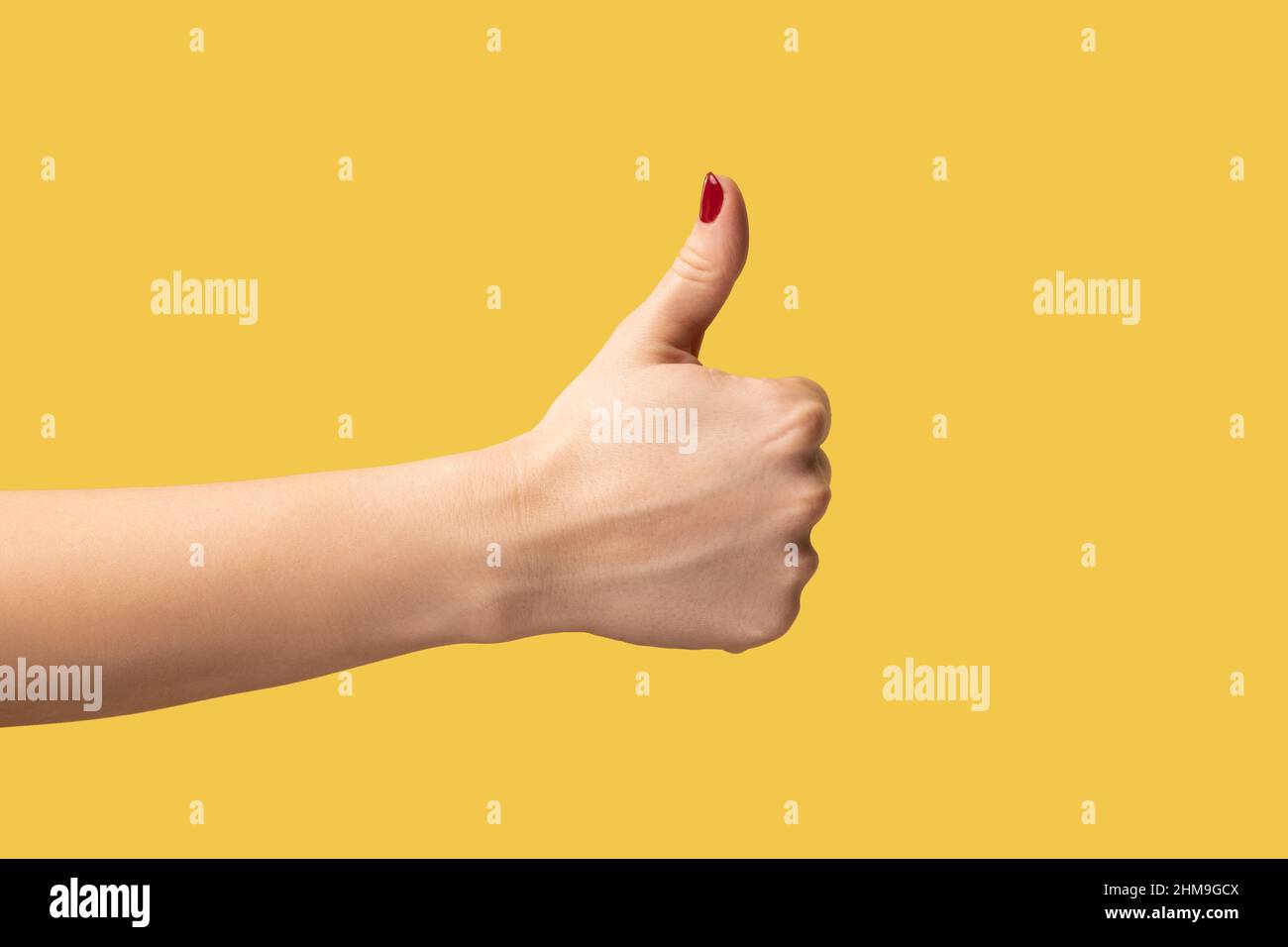 Profile side view closeup of woman hand showing like or thumbs up, approved, positive feedback. Indoor studio shot isolated on yellow background. Stock Photo