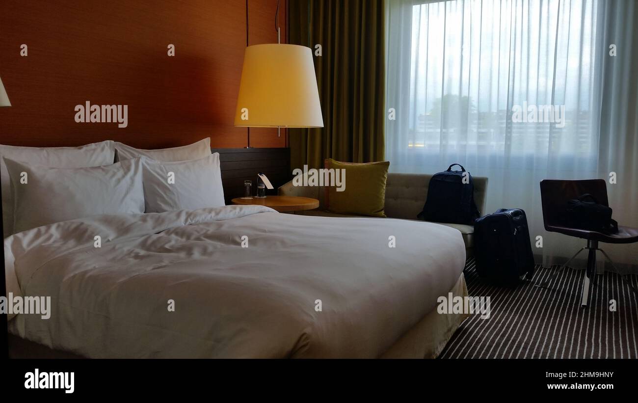 A luxury hotel room with a warm light, bed and a couch is ready for welcoming its guests. Stock Photo