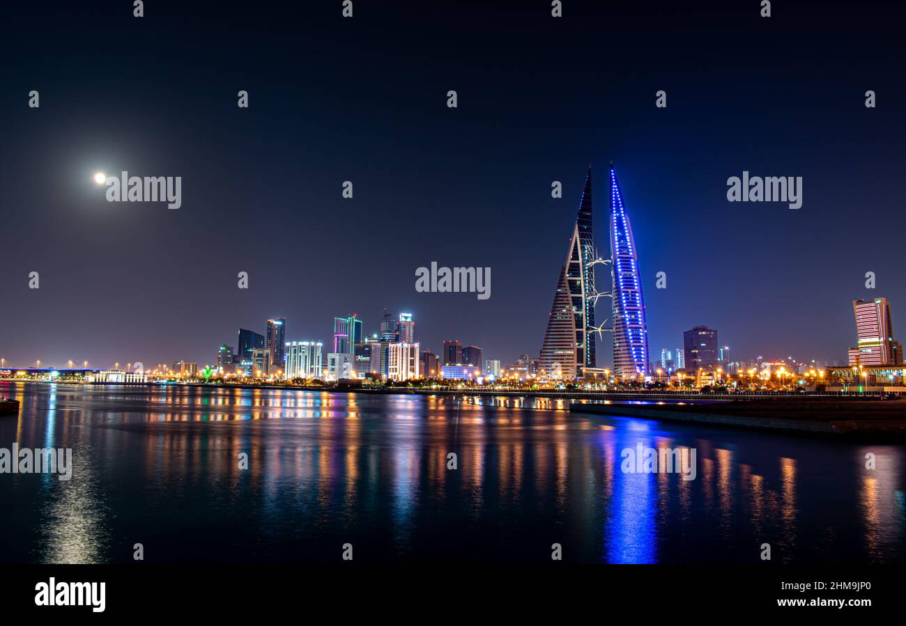 A full moon shines over the skyline of Manama, Bahrain, as the lights for the World Trade Centre and surrounding buildings reflect off the sea. Stock Photo