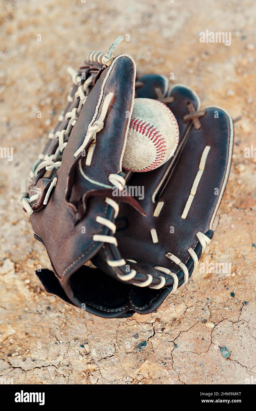 No game is over until the final out is made. Shot of a baseball mitt and ball lying on the pitch during the day. Stock Photo
