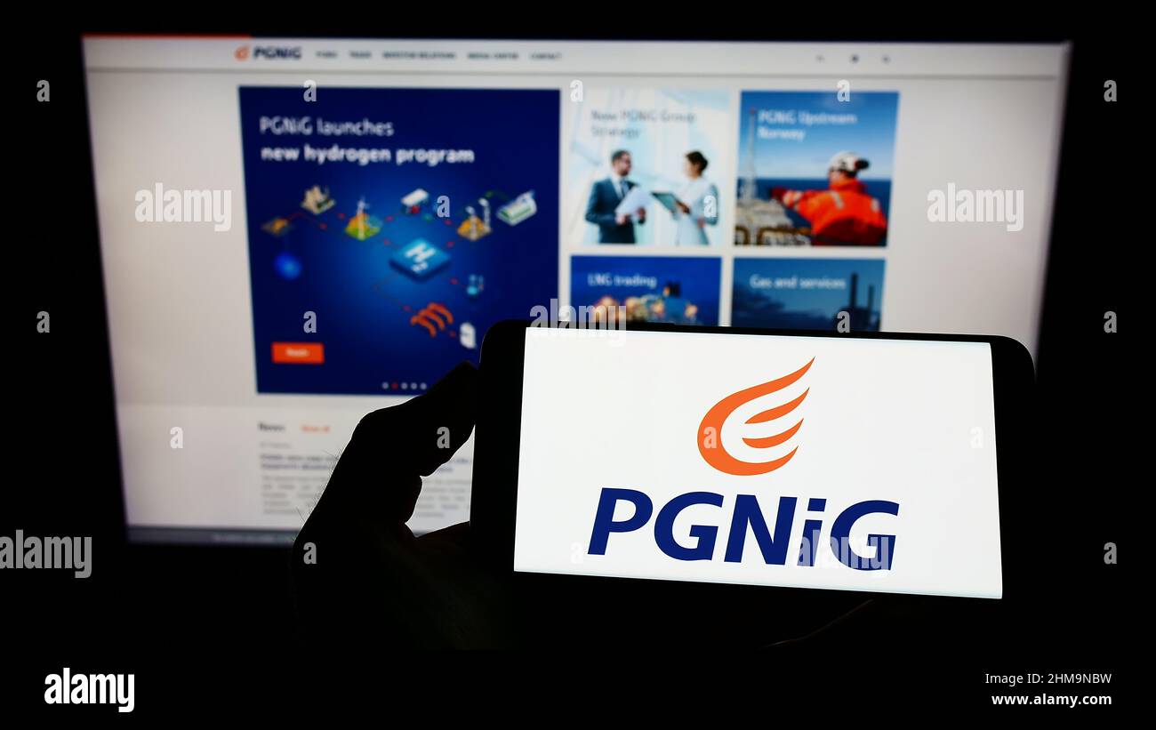 Person holding smartphone with logo of Polskie Gornictwo Naftowe i Gazownictwo S.A. (PGNiG) on screen in front of website. Focus on phone display. Stock Photo