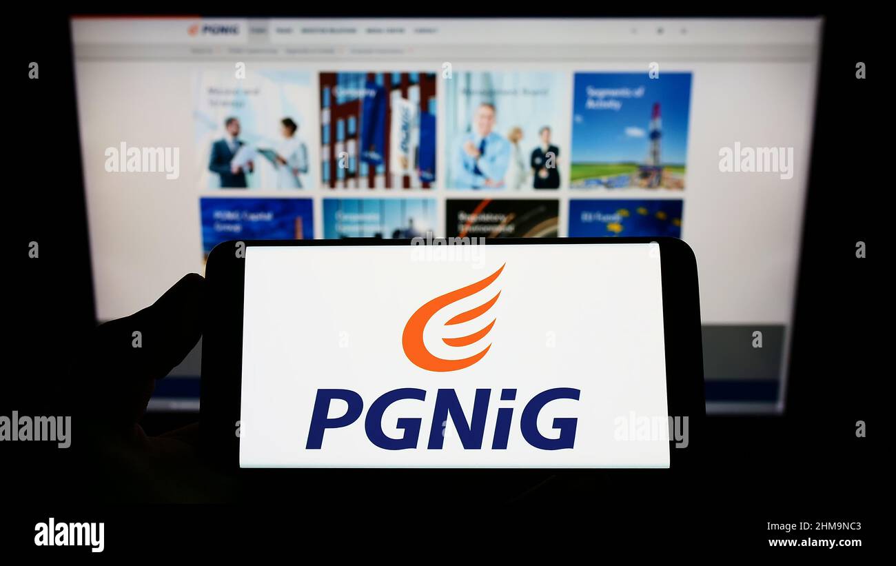 Person holding mobile phone with logo of Polskie Gornictwo Naftowe i Gazownictwo SA (PGNiG) on screen in front of webpage. Focus on phone display. Stock Photo