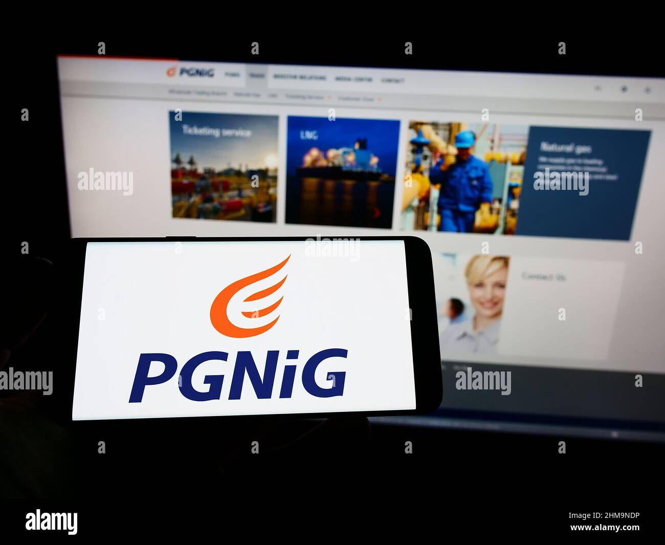 Person holding cellphone with logo of Polskie Gornictwo Naftowe i Gazownictwo S.A. (PGNiG) on screen in front of web page. Focus on phone display. Stock Photo
