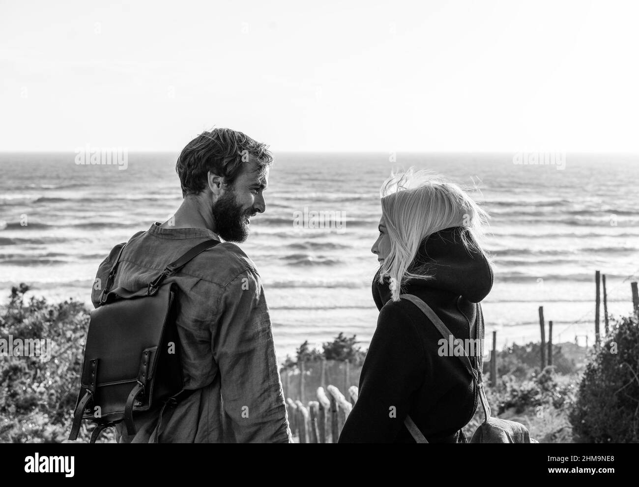 Romantic happy couple in love standing on wooden stairs on dunes at the wild beach in front of the sea - Boyfriend and girlfriend wearing vintage back Stock Photo