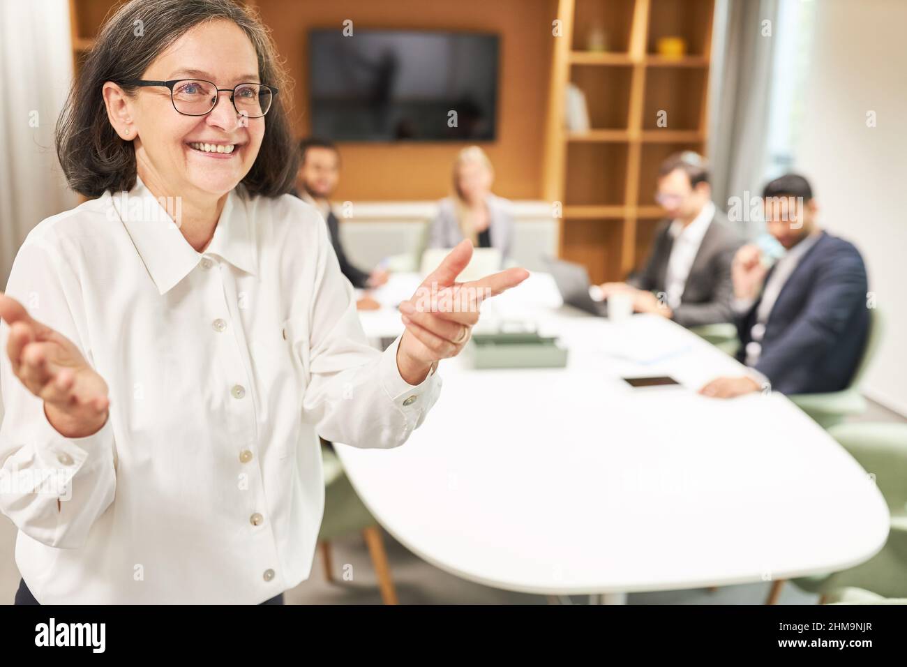 Senior woman as motivational speaker in coaching with business team in conference room