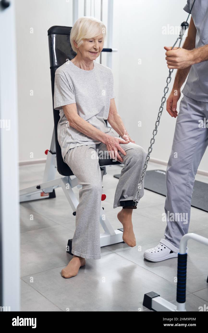 Medical specialist lifting leg of senior citizen with cable machine Stock Photo