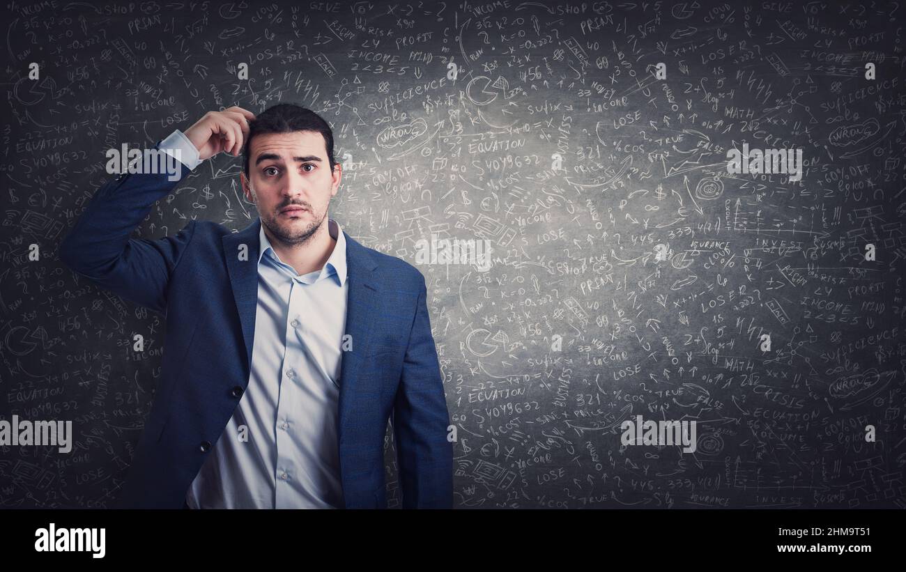 Clueless and pensive businessman scratching his head thinking for solutions on solving difficult calculations. Puzzled male looks confused in front of Stock Photo