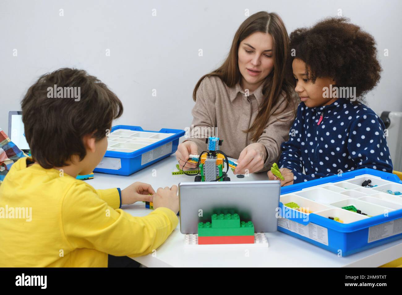 Multiethnic kids at STEM lesson constructing robot in classroom with woman teacher Children making electronic arm model at modern science school Stock Photo