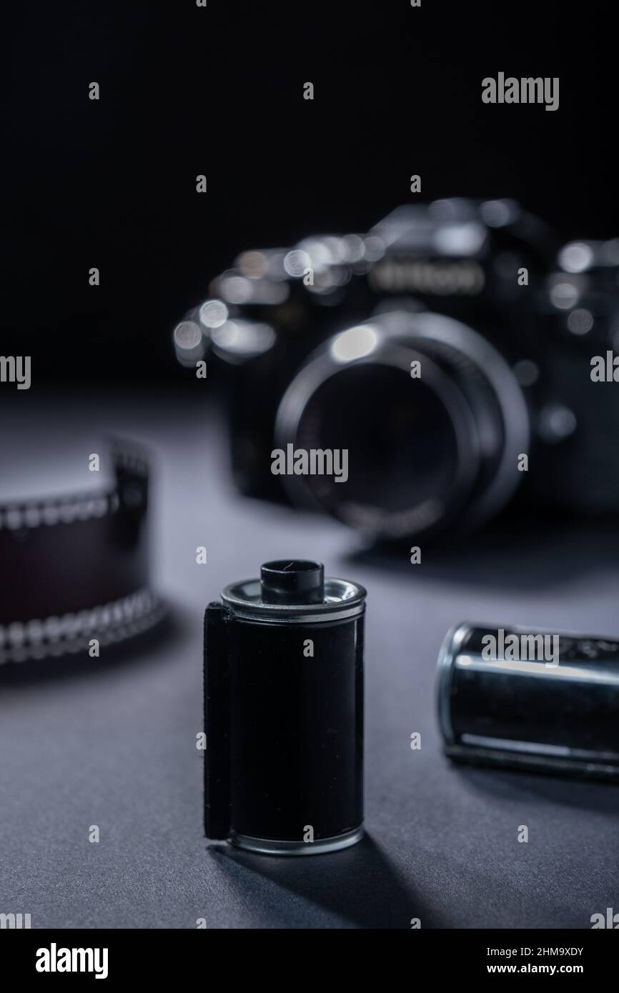 Film photography - a vintage metallic film cartridge and 35mm SLR camera against a dark background. Stock Photo