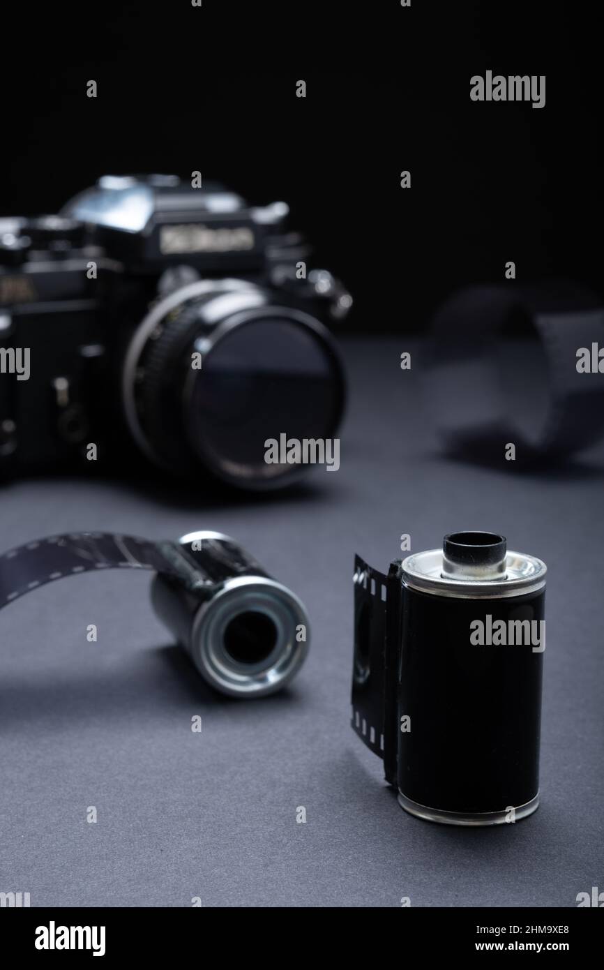 Film photography - a vintage metallic film cartridge and 35mm SLR camera against a dark background. Stock Photo