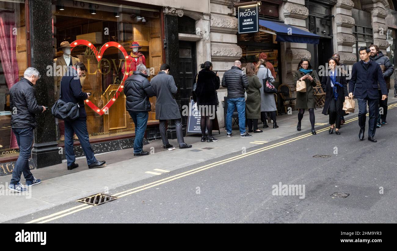 London, UK.  8 February 2022.  Office workers form a long queue outside Piggys, a popular sandwich bar in Air Street.  As Plan B restrictions have been relaxed, office workers are returning to the workplace and lunchtime queues are becoming more and more common.  Credit: Stephen Chung / Alamy Live News Stock Photo