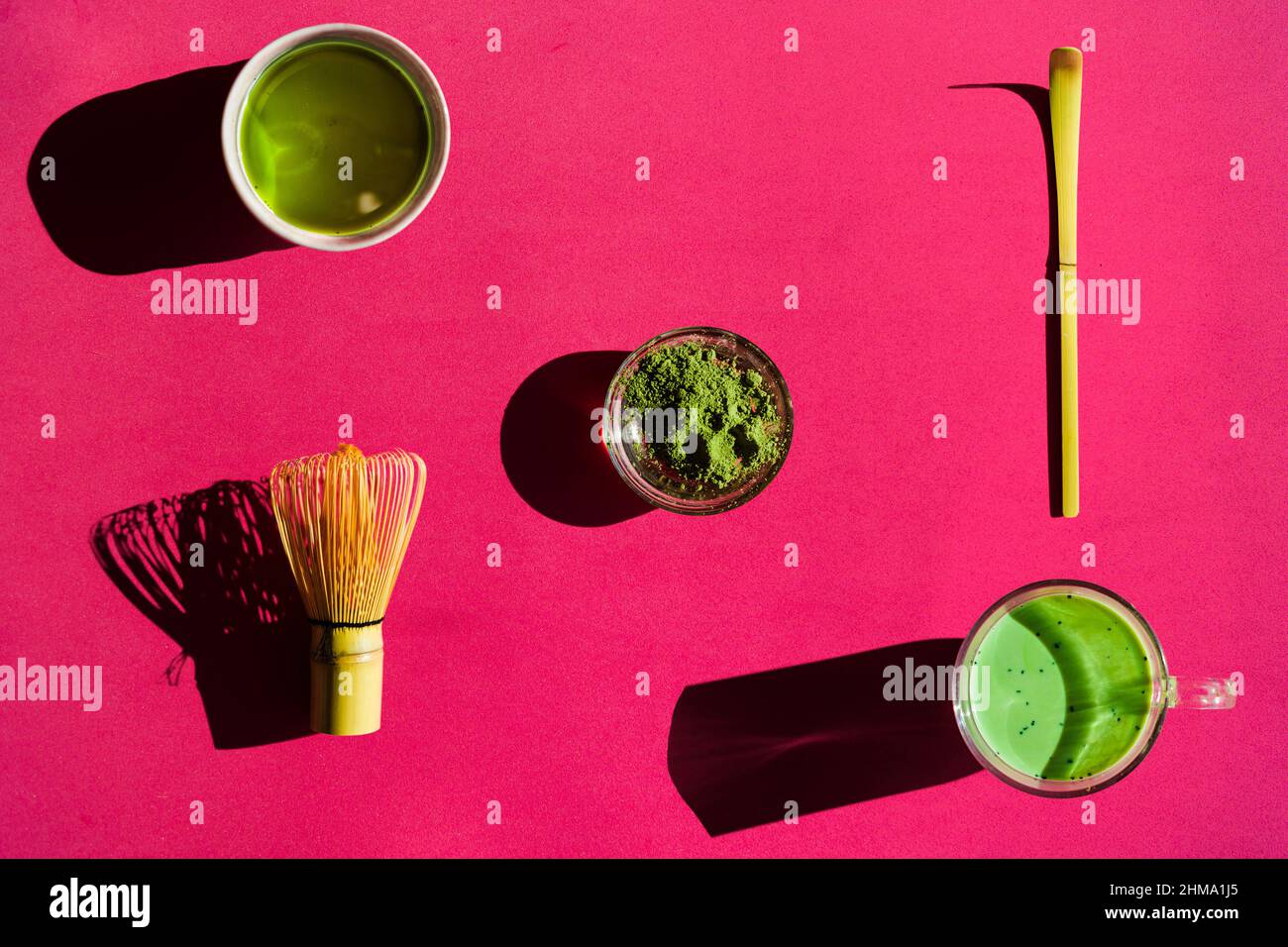 Top view of bright background of glass of green tea and dried matcha with bamboo chasen and chashaku on pink surface Stock Photo