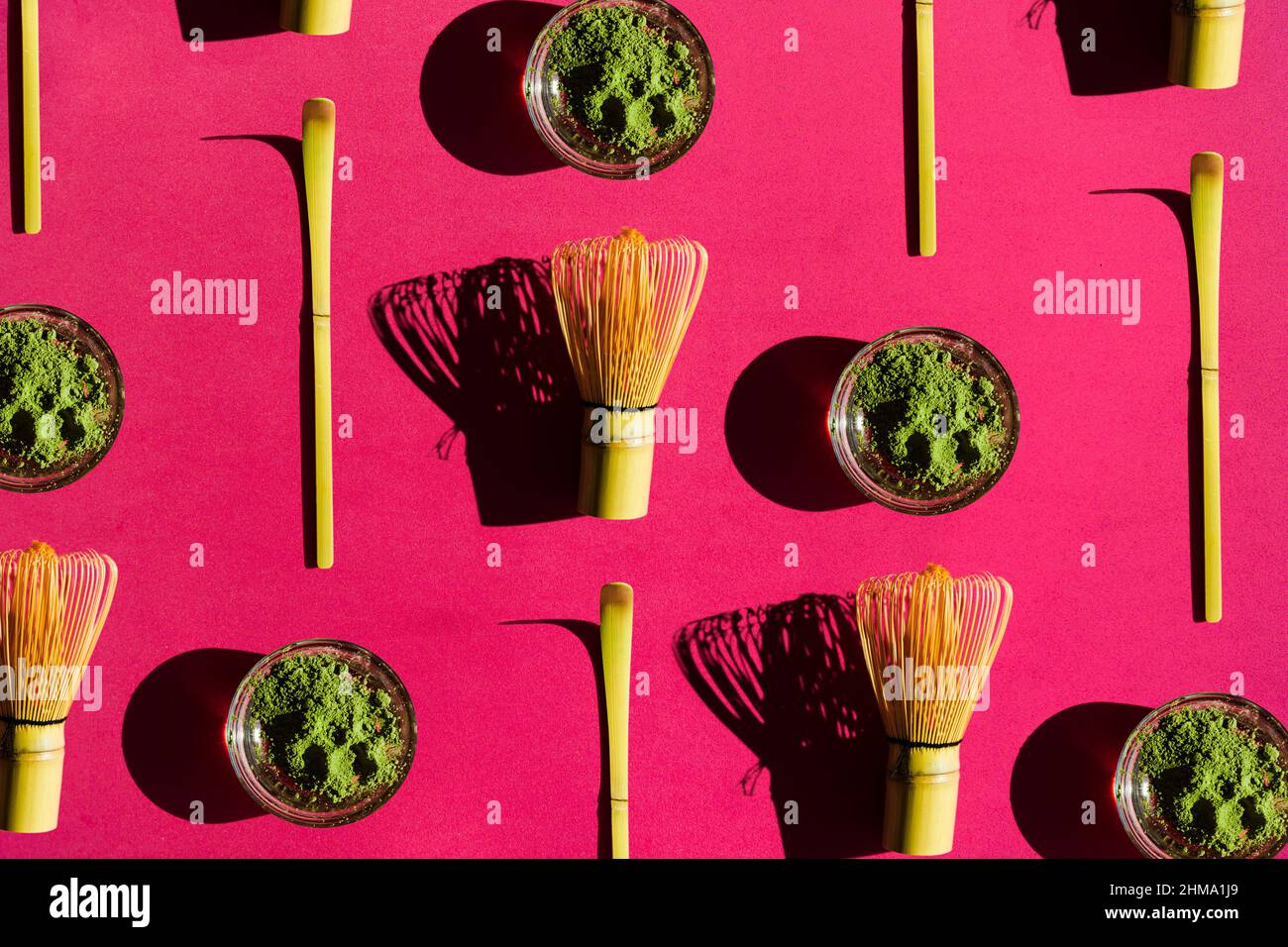 Top view full frame bright background of glass of green tea and dried matcha with bamboo chasen and chashaku on pink surface Stock Photo