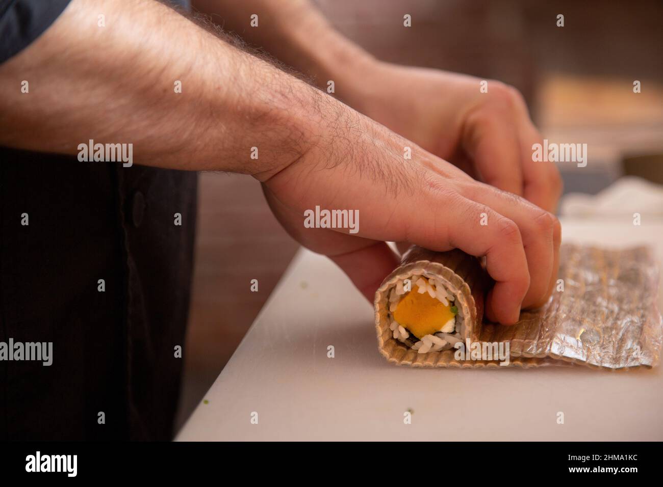 Crop anonymous male chef using bamboo mat while rolling fresh uramaki sushi with radish during work in restaurant on blurred background Stock Photo