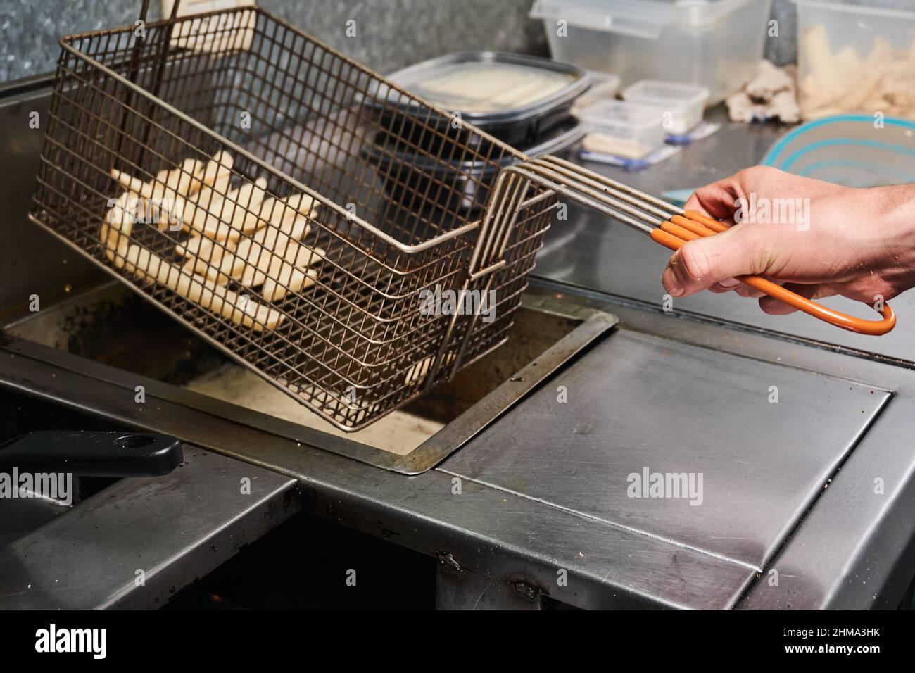 Side view of anonymous cook preparing French fries in deep fryer while