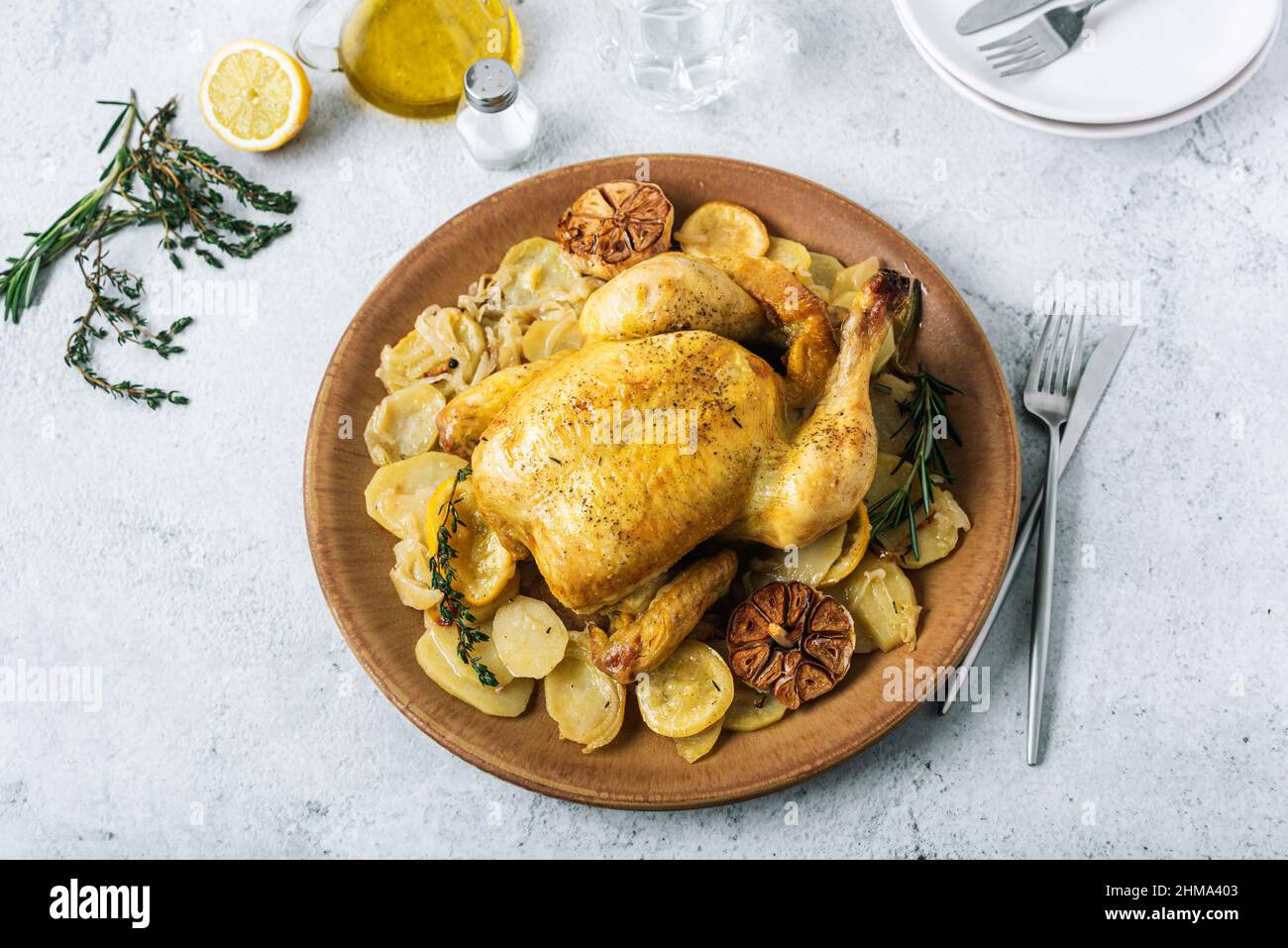 From above of ceramic plate with roasted chicken garnished with slices of roasted potatoes and seasoned with fresh rosemary and different spices Stock Photo