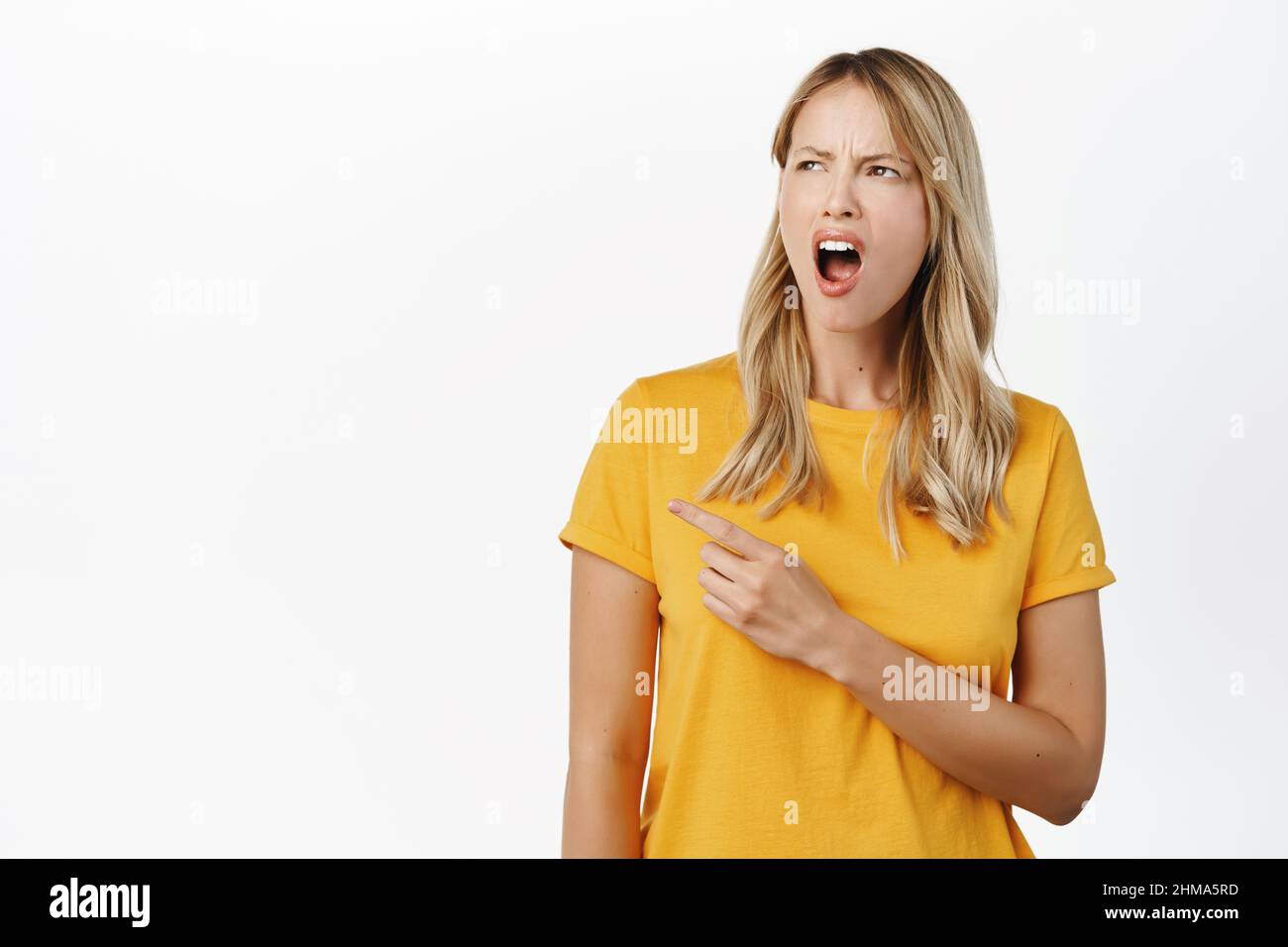 Portrait of angry blond girl pointing and looking left with frustrated ...