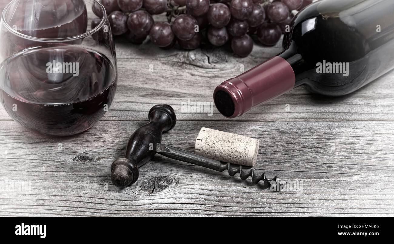 Antique corkscrew with a bottle of red wine, grapes, and drinking glasses in background on rustic wood table with vintage effect Stock Photo