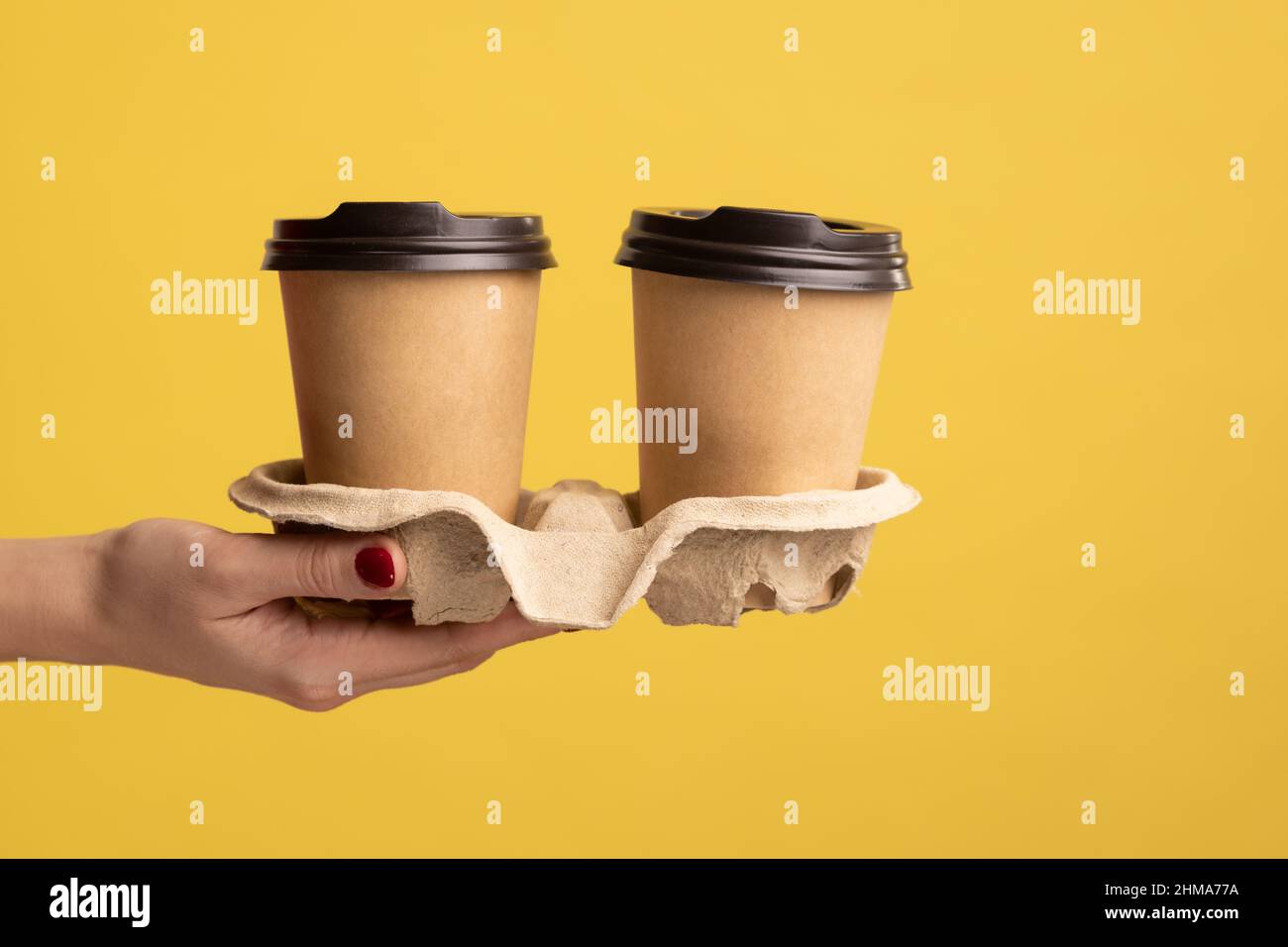 Profile side view closeup of woman hand holding and showing cup of hot takeaway mug drink in hand, coffee break at work. Indoor studio shot isolated on yellow background. Stock Photo