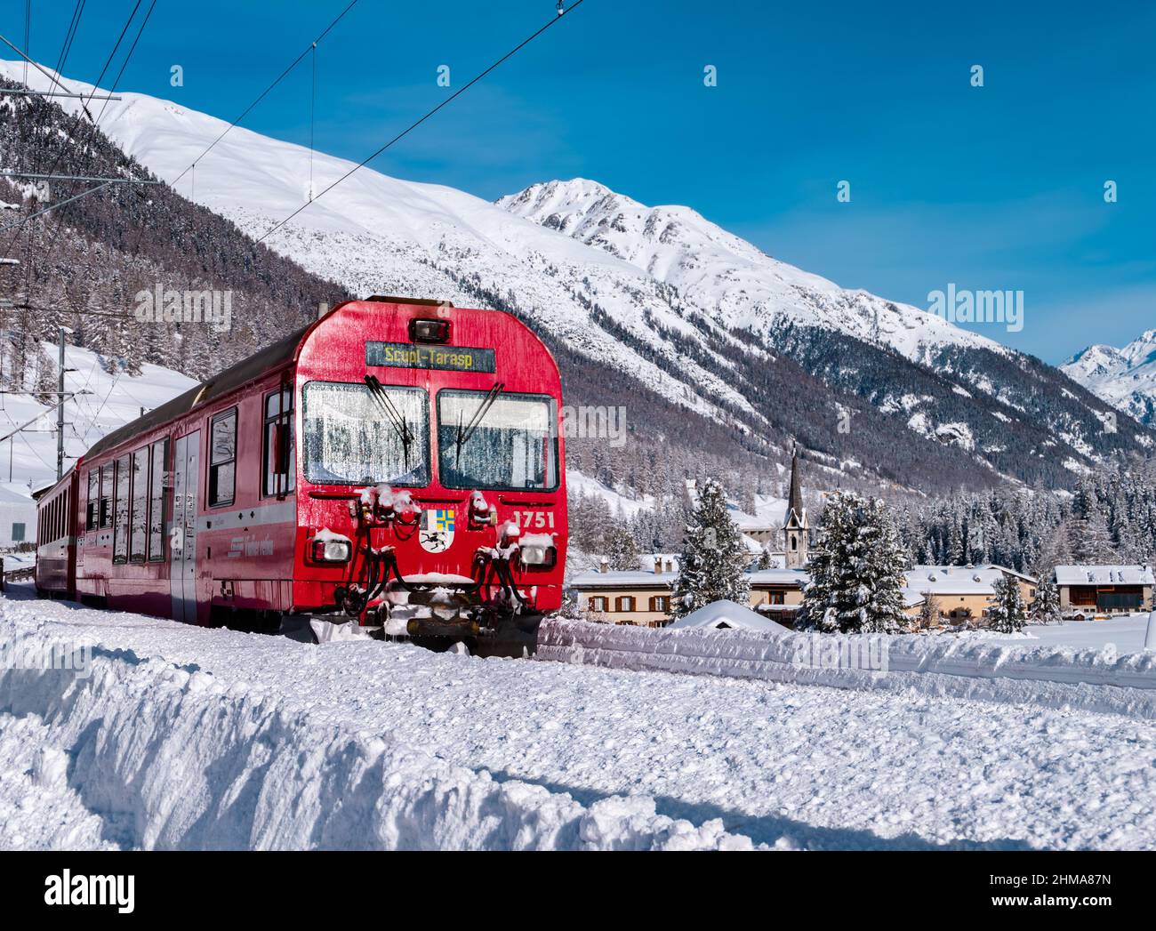 Cinuos-Chel, Switzerland - February 3, 2022: Red train riding between Chur and Tirano in Italy and crossing snow covered landscape at the village Chin Stock Photo