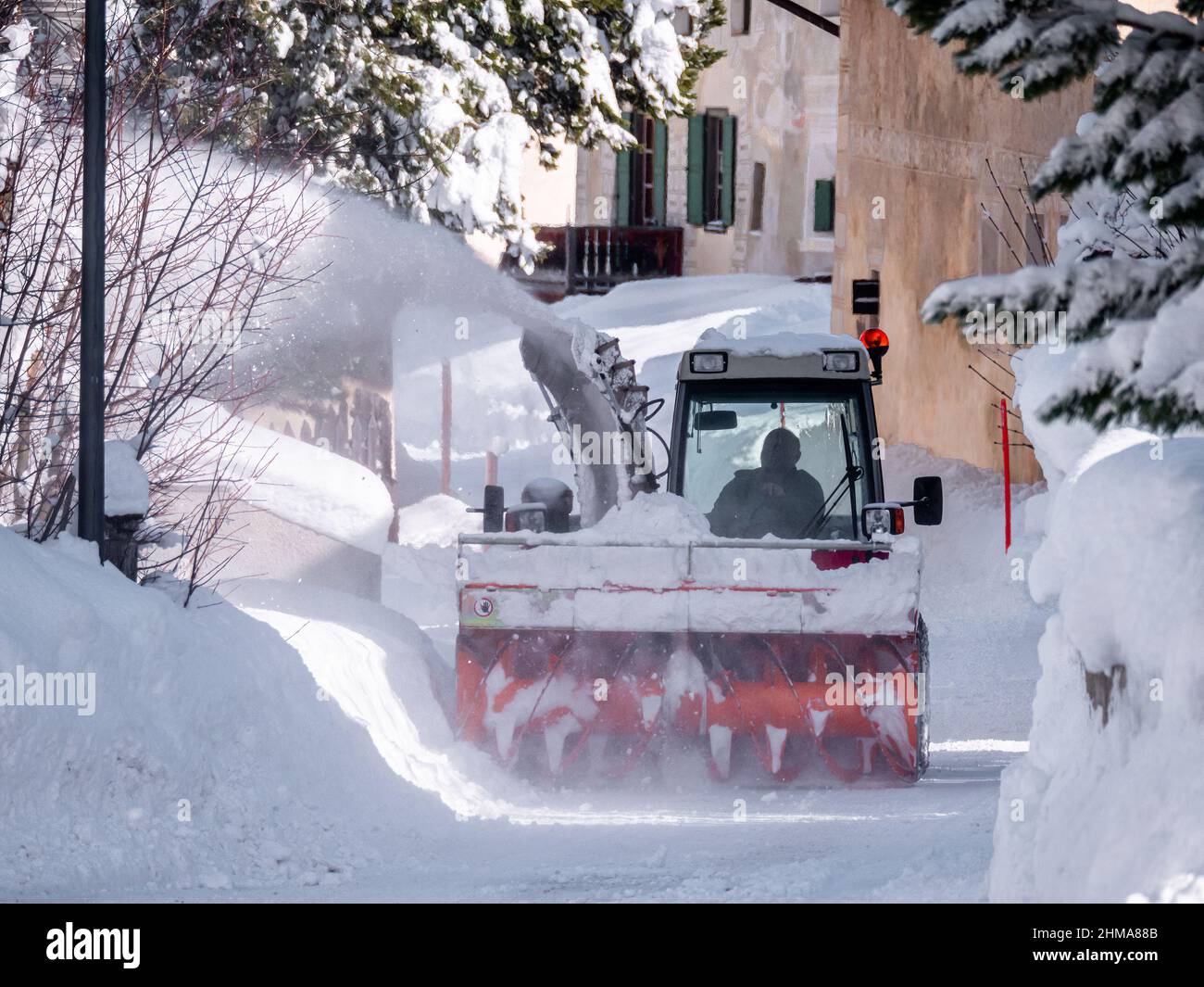 Cinuos-Chel, Switzerland - February 3, 2022: A snow plow vehicle clears a snowy road in the old traditional Swiss village of Cinuos-Chel in Engadine, Stock Photo