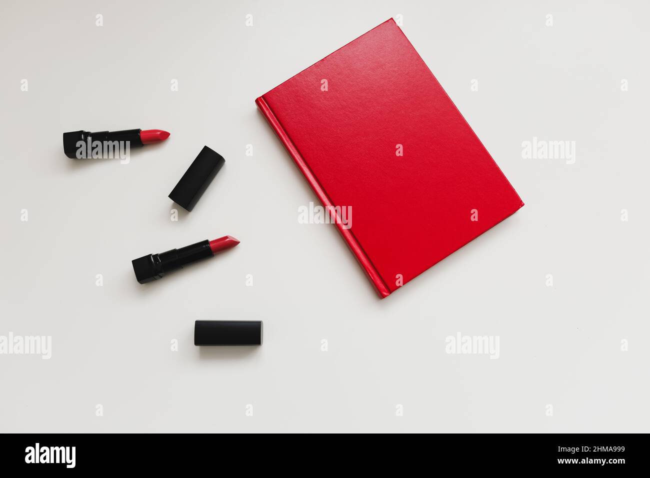 Feminine desk with cosmetics, lipstick and red book or diary on white