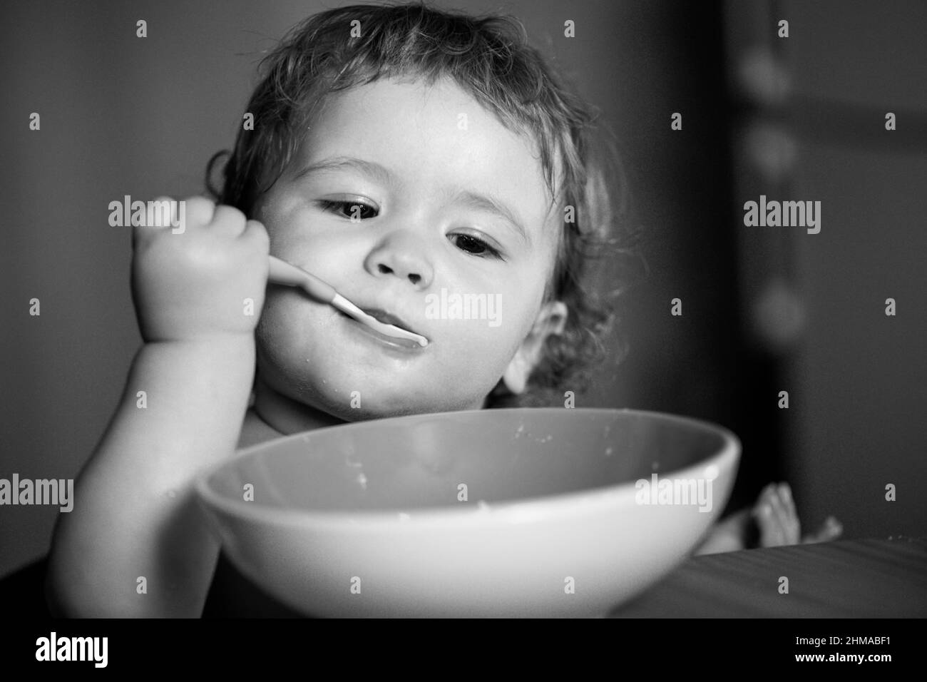 Portrait of funny little baby boy eating from plate holding spoon ...