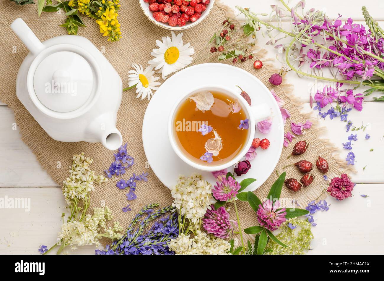 Herbal tea with rosehip, chamomile and meadowsweet in a white cup on a white wooden table with flowers, flat lay Stock Photo