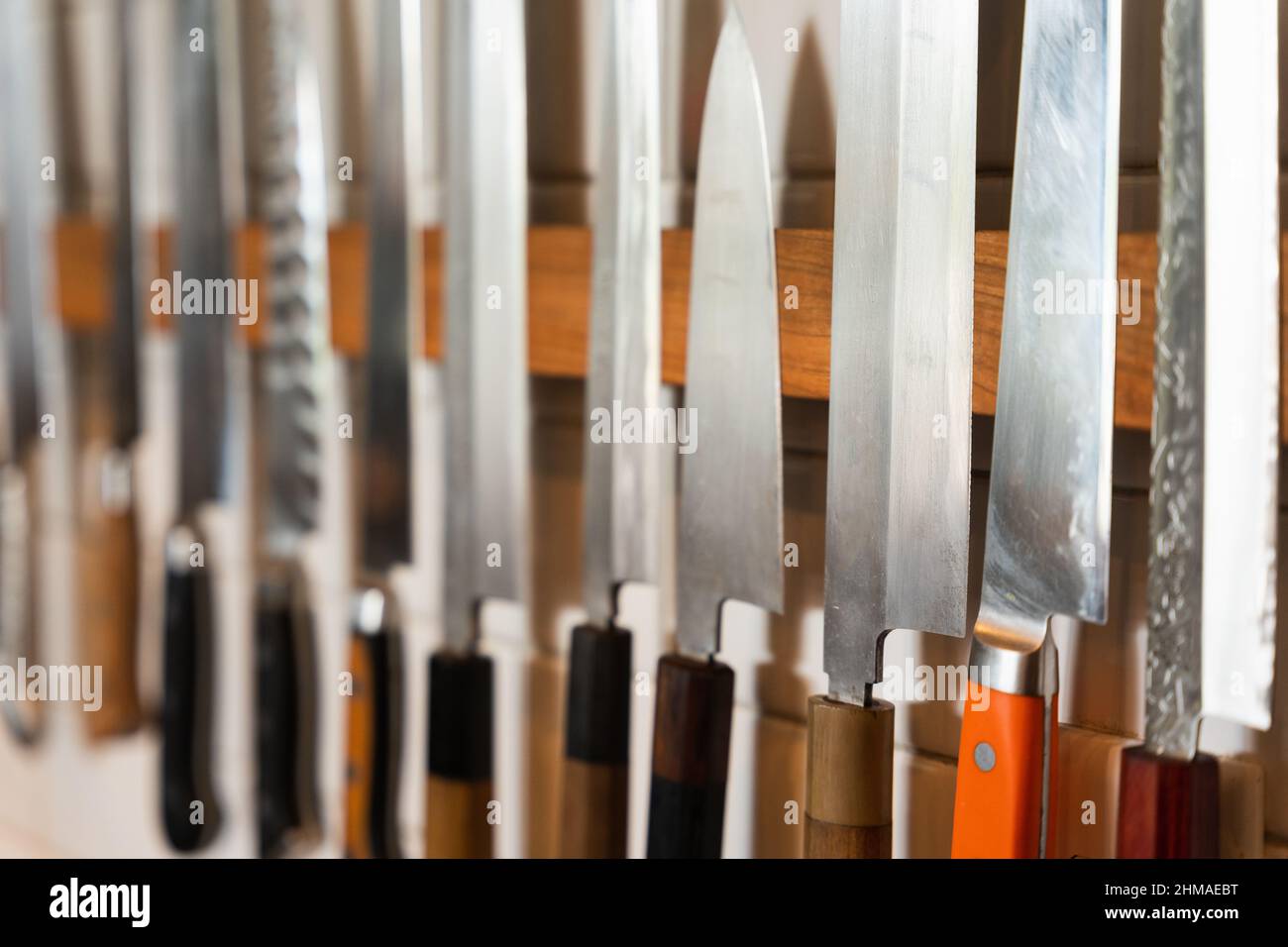 Closeup of assorted sushi knives along a restaurant wall Stock Photo