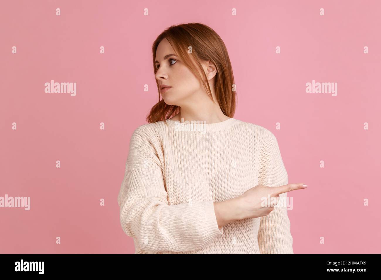 Go away. Portrait of blond woman showing exit, demanding to leave her alone, turning away with resentful irritated expression, wearing white sweater. Indoor studio shot isolated on pink background. Stock Photo