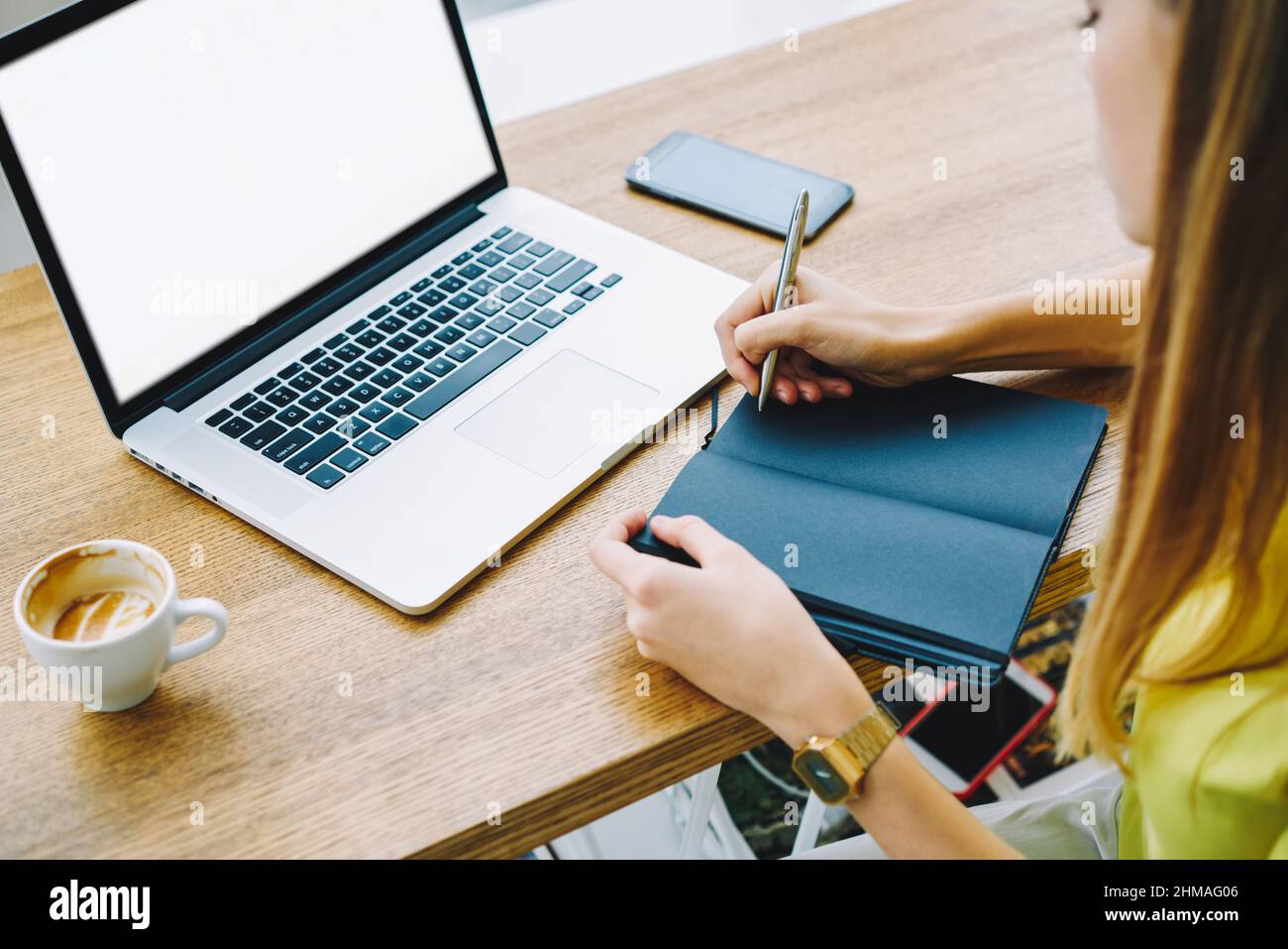 Unrecognizable lady working on laptop while making notes in notepad Stock Photo