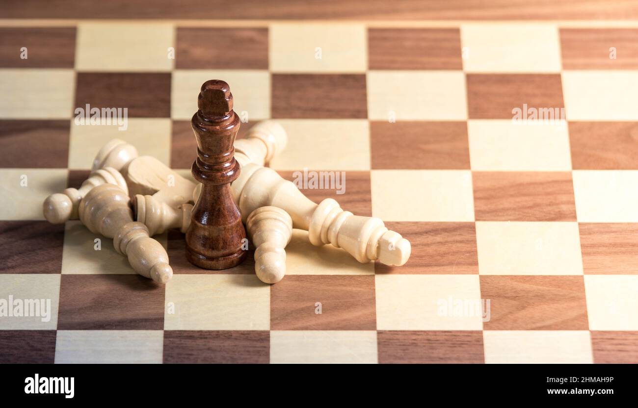 Fallen Chess pieces lying around a King on a chess board. Light shining from right side Stock Photo