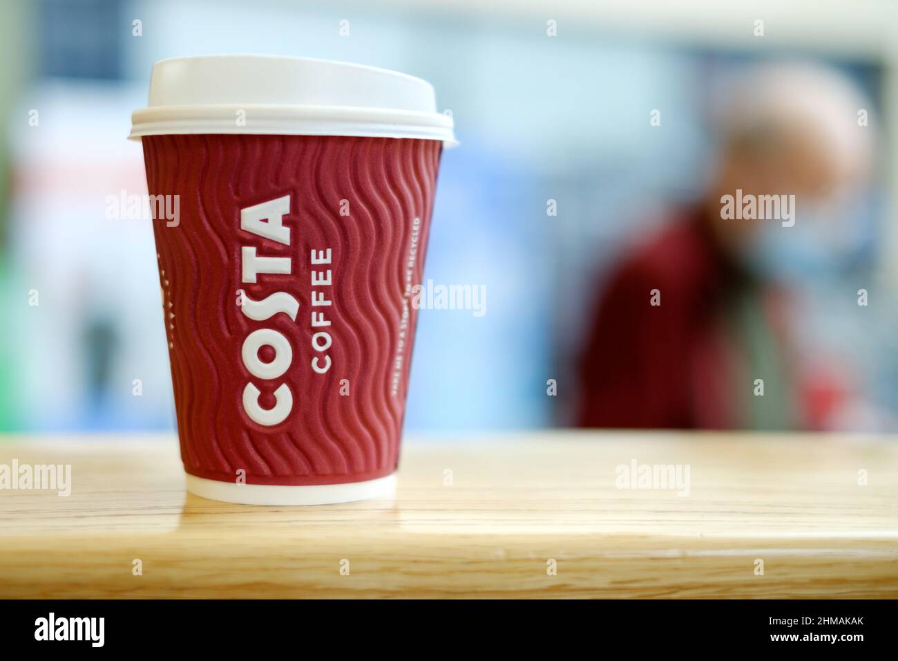 A Costa Coffee disposable cardboard cup with a plastic lid sits on a table. The company has worked hard to make their throw away cups more sustainable Stock Photo