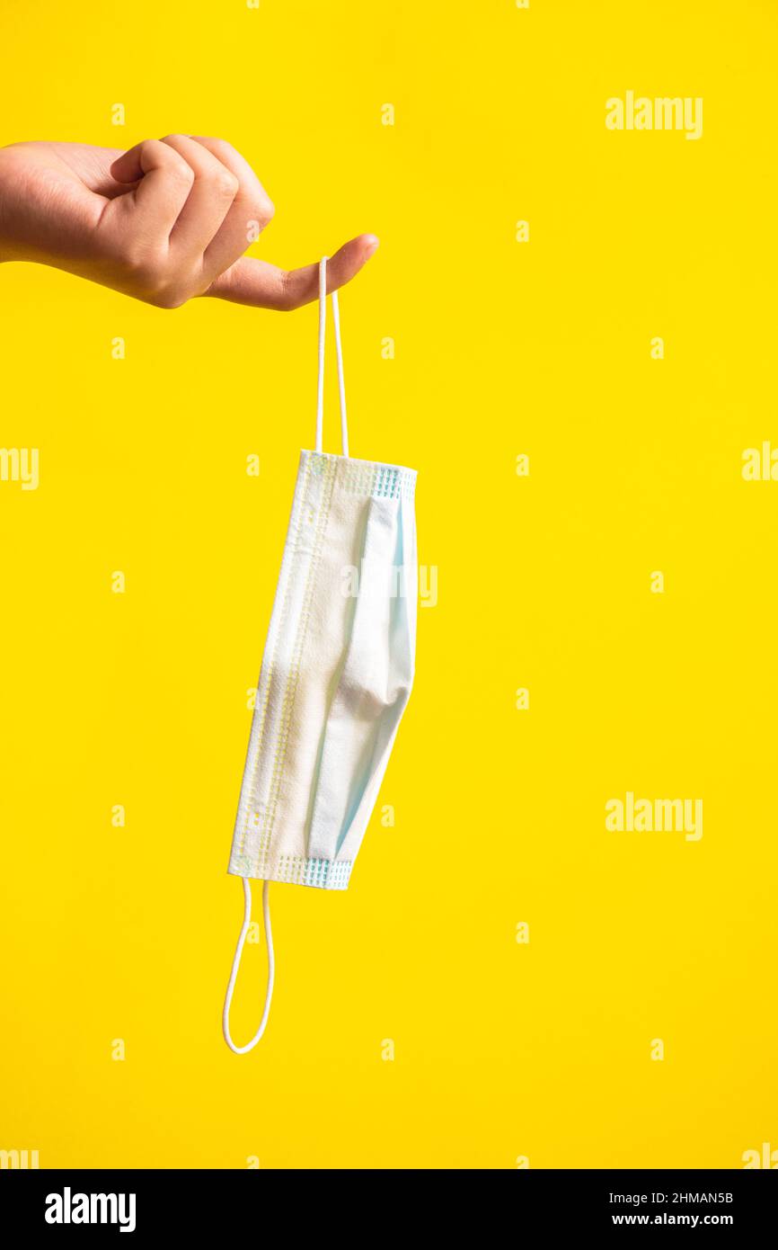 Medical mask in a girl's hand. Yellow background. Stock Photo