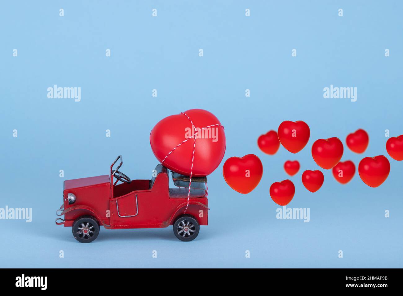 Red retro car carrying a lot of hearts for Valentine's day on bright blue background. Creative concept of love. Copy space Stock Photo