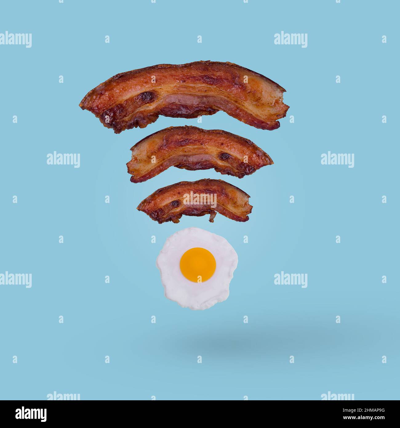 Wi fi symbol creative idea made of fried egg and slices of crispy bacon on blue color background. Minimal food idea and Internet technology /networkin Stock Photo