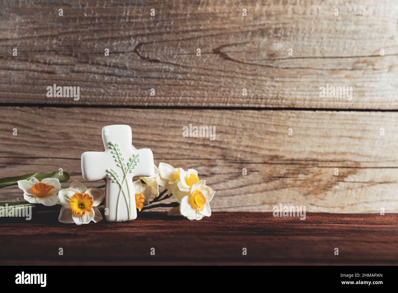 Easter holiday conceptual background on rustic wooden boards. Photo of gingerbread cookie Cross shape, narcissus or daffodils flowers on table top. Card with copy space to place text. Minimal concept Stock Photo