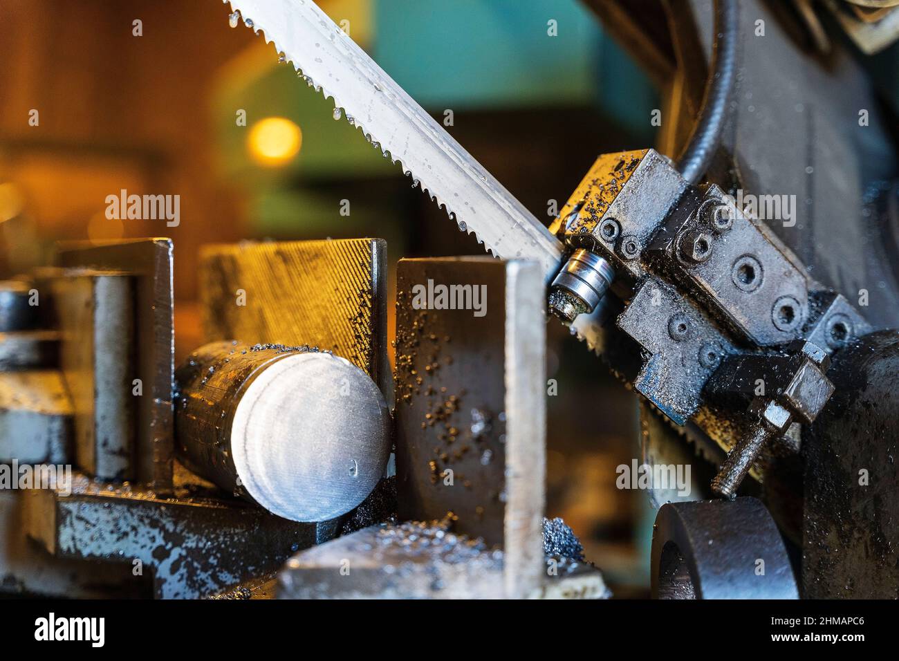 A metal band saw in the cuts a metal rod with a liquid