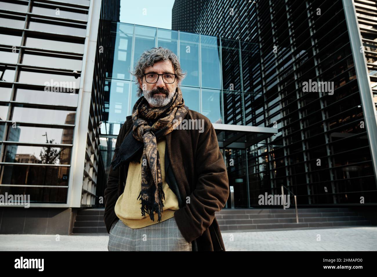 Middle-aged man looking at the camera while posing in the financial district with an office building on background. Stock Photo