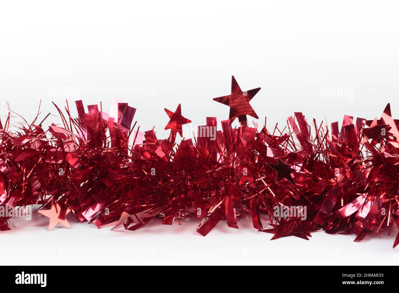 Red Christmas tinsel with stars. It is located on a white surface. Close-up. Stock Photo