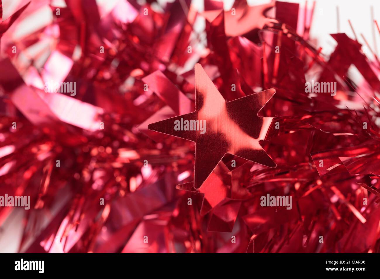 Red Christmas tinsel with stars. It occupies the entire surface of the image. Close-up. Stock Photo